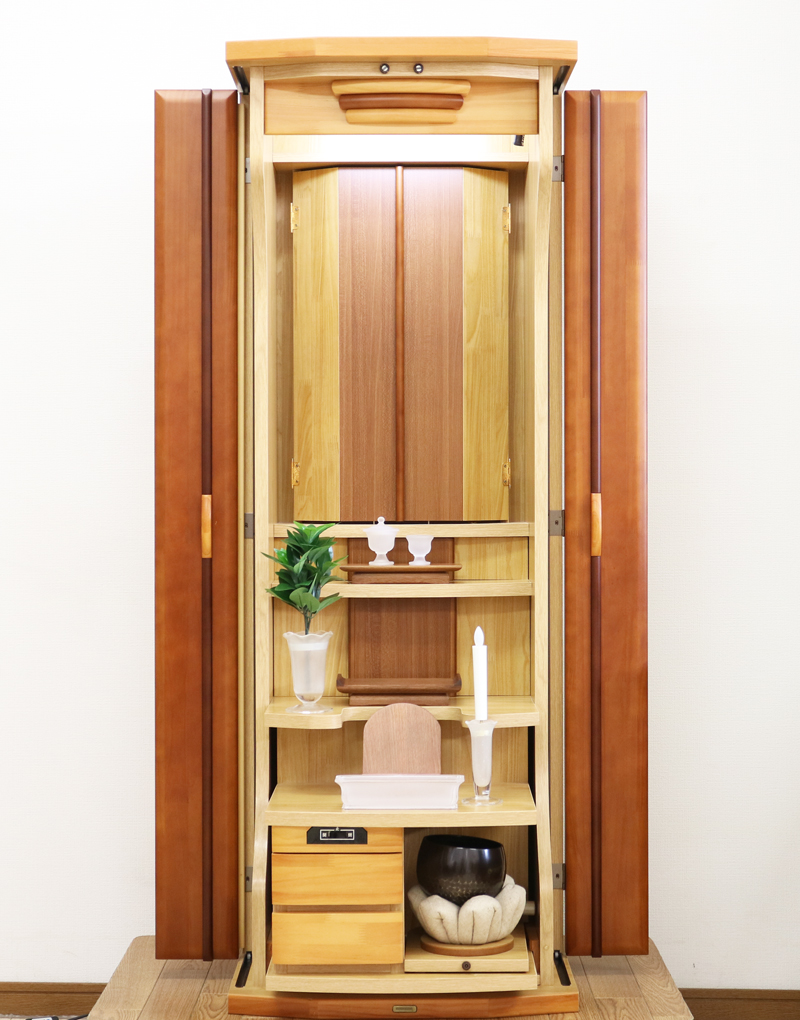  ダーク色とライト色のツートンのコンビネーション色です。今までのお仏壇のデザインではなかった、オシャレな雰囲気漂うデザインに仕上がっております。  材質はデザインにあった、パイン材を使用しており、暖かみあふれる明るい印象をお部屋にプラスしてくれます。  金剛堂アンサンブル現在でも販売されているお仏壇です。    製品名 創価学会中古仏壇709 設置 	和室・洋室・拠点・ワンルーム・一人暮らしにも最適です 種別 	家具調仏壇 サイズ 	  仏壇全体:高さ145cm x 幅54cm x 奥行き49cm  扉二つ折り最大幅:79cm  厨子内寸: 52cm x 32cm 	  材質 	芯材:MDF、扉:パイン材、 機能 	  自動扉・引き出し3箇所(厨子下一個、下部引き出し二個)、収納経机